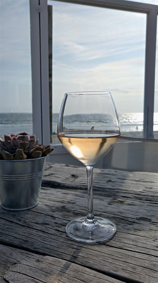 Ein Glas Roséwein auf einem Holztisch mit Blick aufs Meer