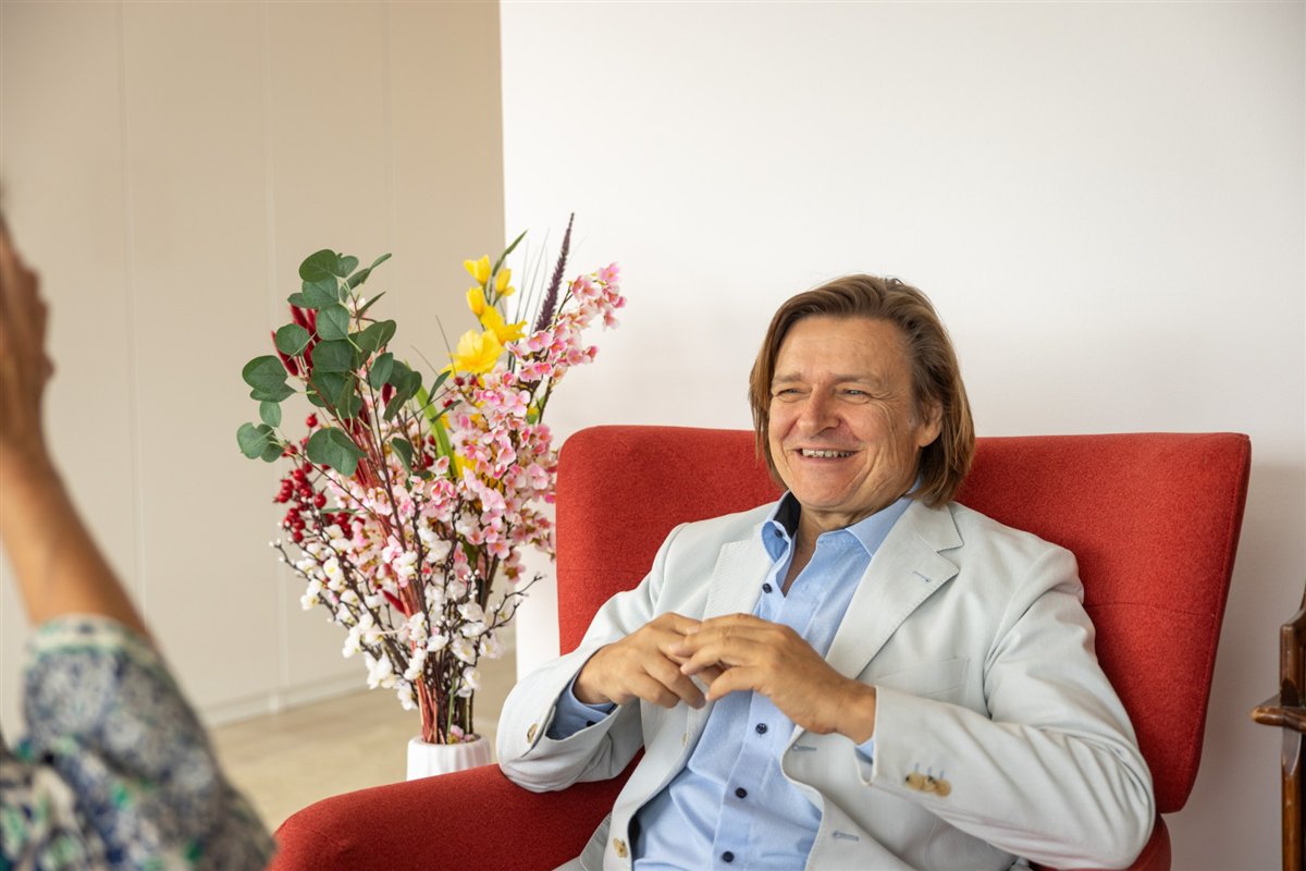 Dr. Ralf Hillemacher lacht im Gespräch, im roten Sessel sitzend