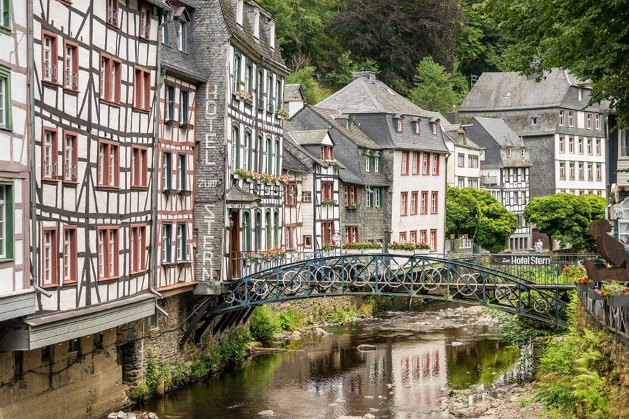 Fachwerkhäuser an einem Fluss mit einer Fußgängerbrücke in der Eifel