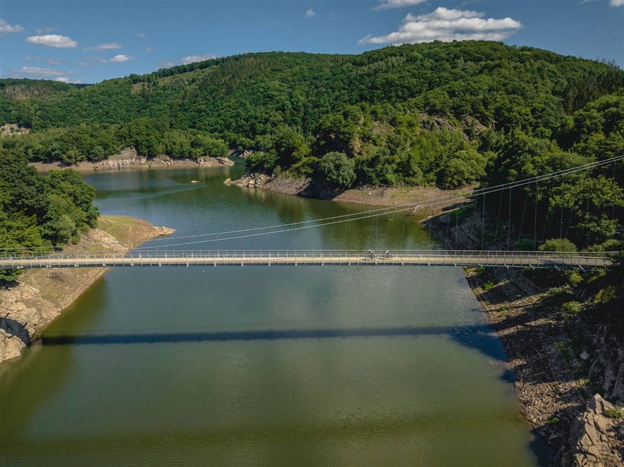 Hängebrücke über einem See mit zwei Radfahrern